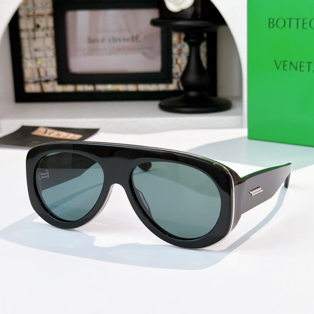 Black oversized sunglasses with teal-blue lenses and green-accent temples.