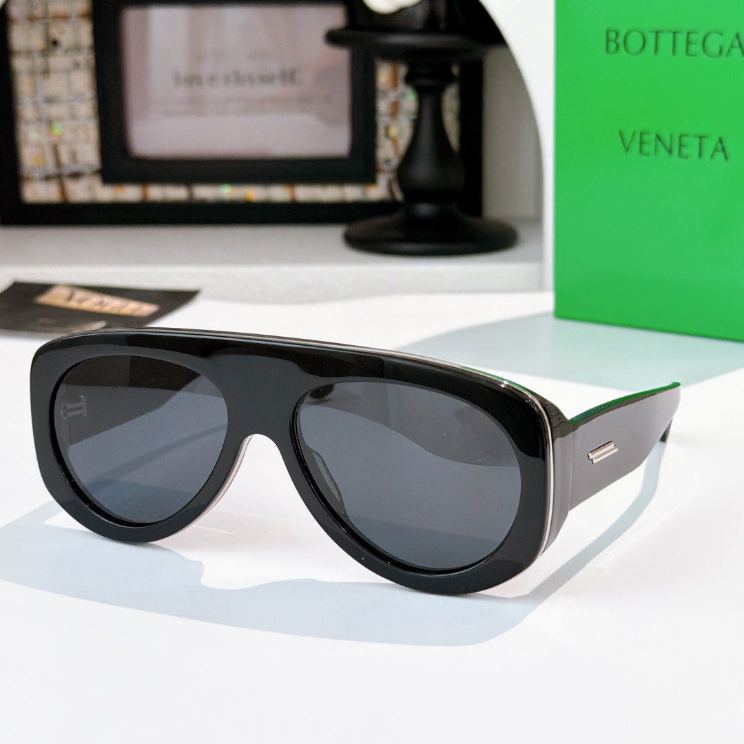 Black oversized sunglasses with dark gray lenses and green-accent temples.