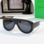 Black oversized sunglasses with dark gray lenses and green-accent temples.