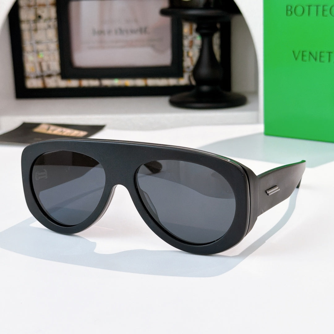 Black oversized sunglasses with dark gray lenses and green-accent temples.