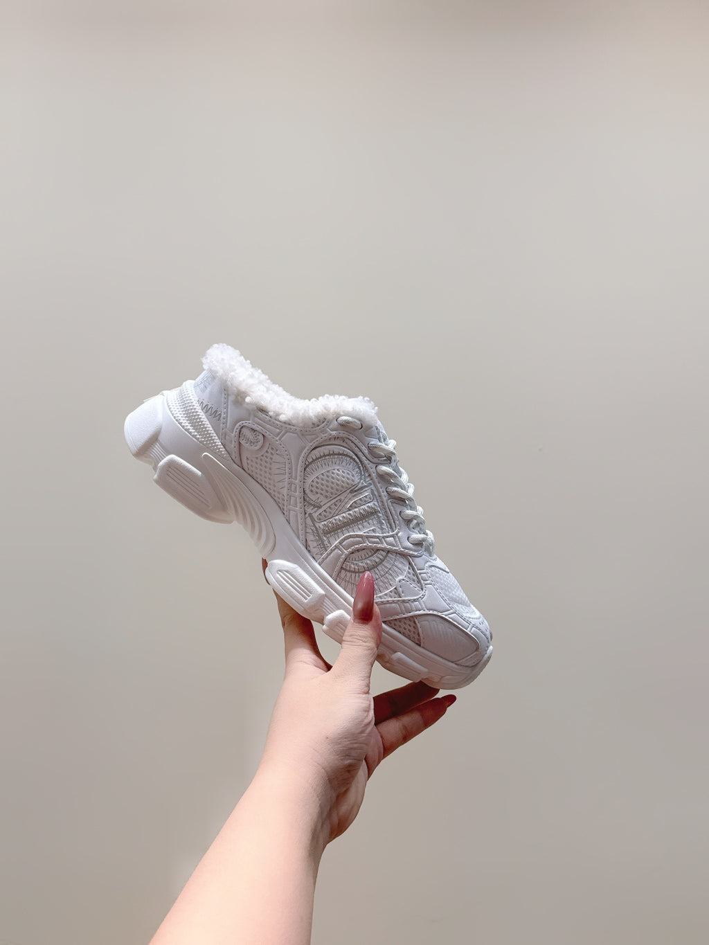 White sneaker held up showing lace-up upper, fuzzy collar, and cushioned outsole