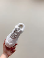 White fur-lined sneaker held in hand, showing lace-up front and textured toe panel