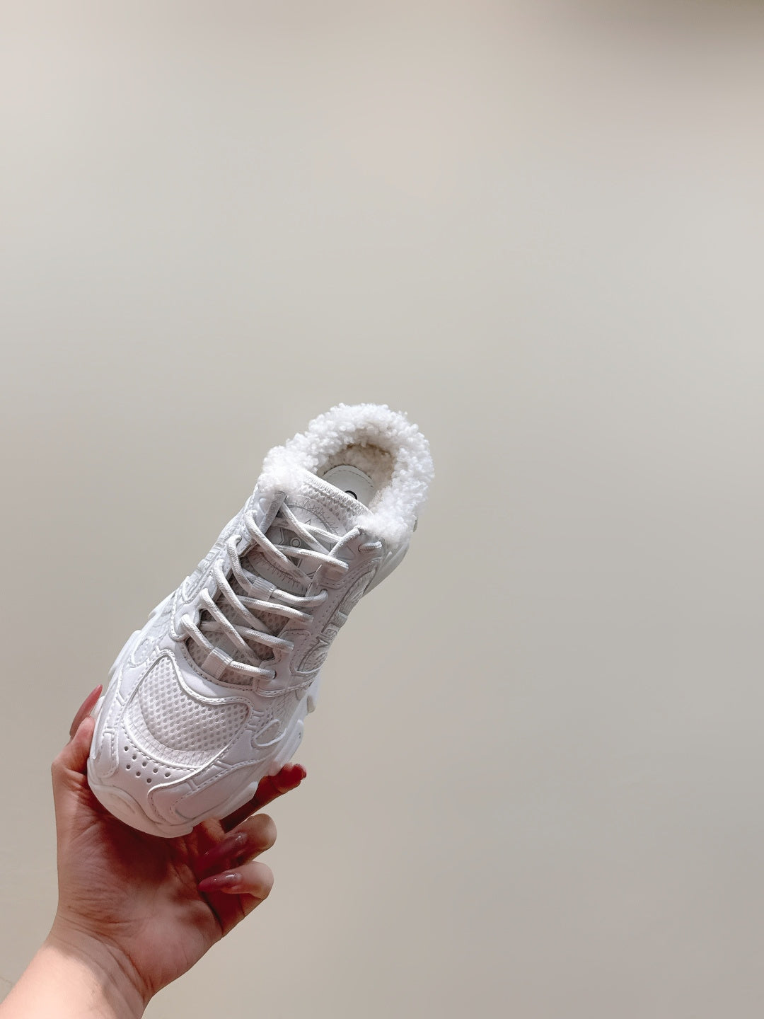 White fur-lined sneaker held in hand, showing lace-up front and textured toe panel