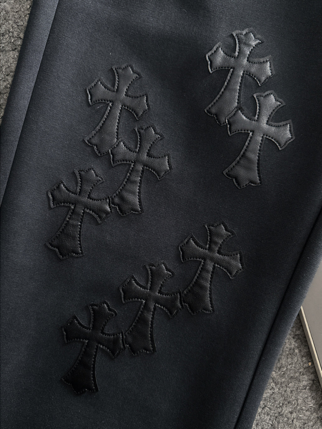 Dark pants with stitched cross embroidery on the front