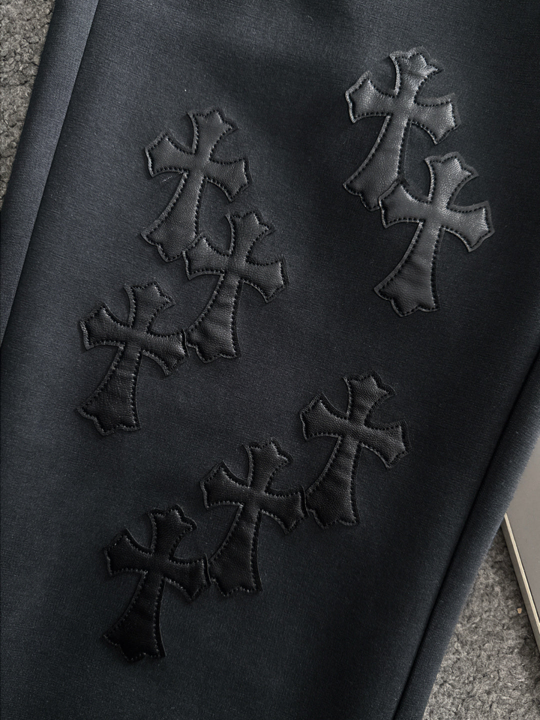 Dark pants with stitched cross embroidery on the front