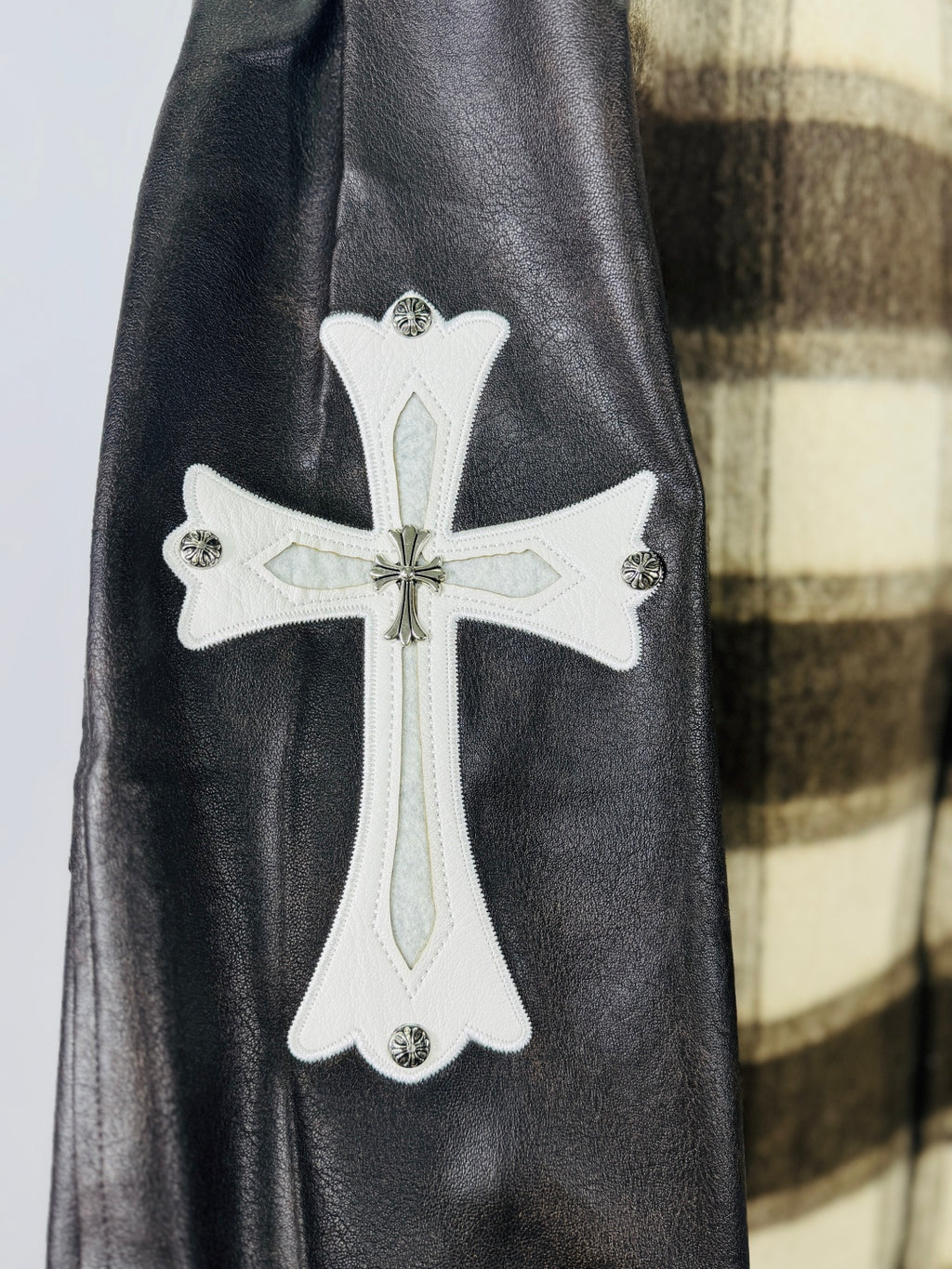 White cross applique patch on black leather sleeve of plaid varsity jacket