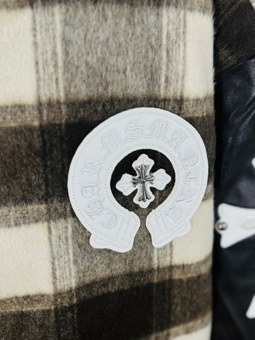 Large white crest patch on plaid varsity jacket front, black sleeve panel visible