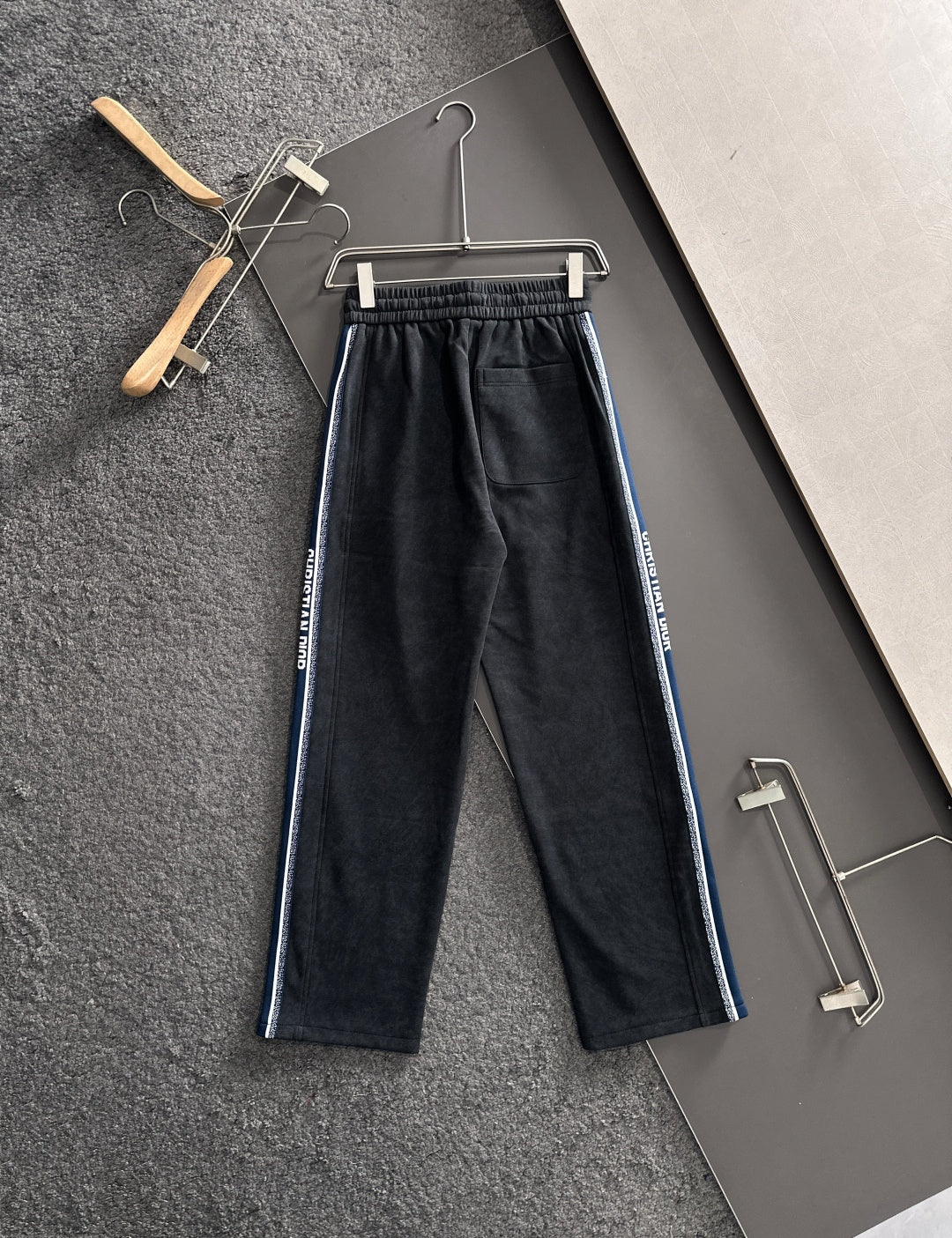 Dior pants on hangers, dark fabric with elastic waist, drawstring, and blue side stripes