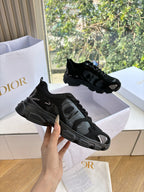 Black lace-up sneakers on display, hand holding one shoe by the sole