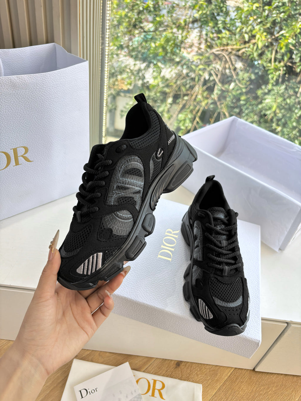 Black lace-up sneakers with textured upper and chunky sole, one held up