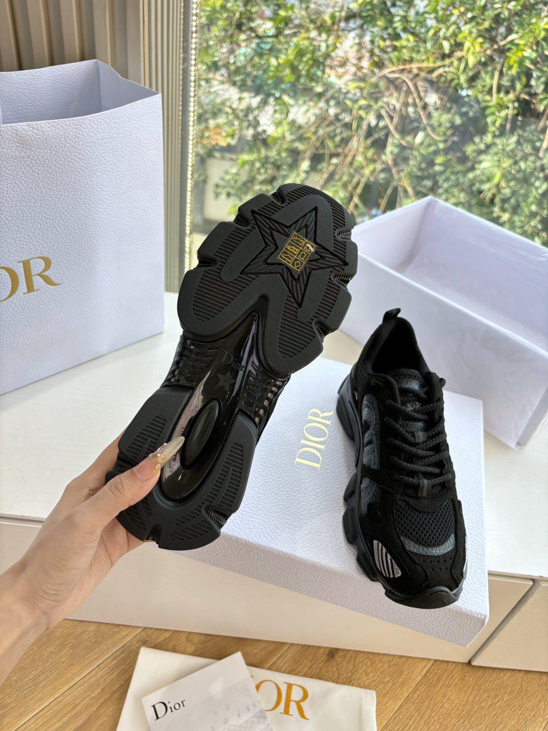 Black sneakers showing outsoles and heels, pair in white shoe boxes
