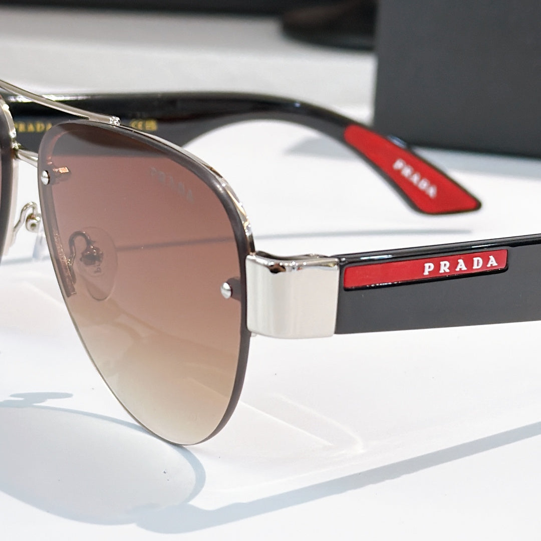 Close-up aviator sunglasses with brown lenses, silver frame, and black/red logo temple