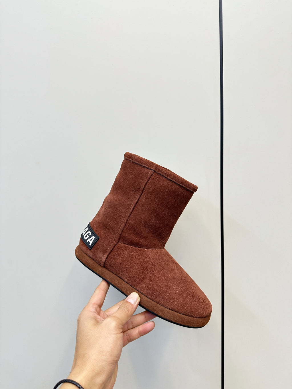 Brown suede ankle boot held in hand, padded collar with side logo patch