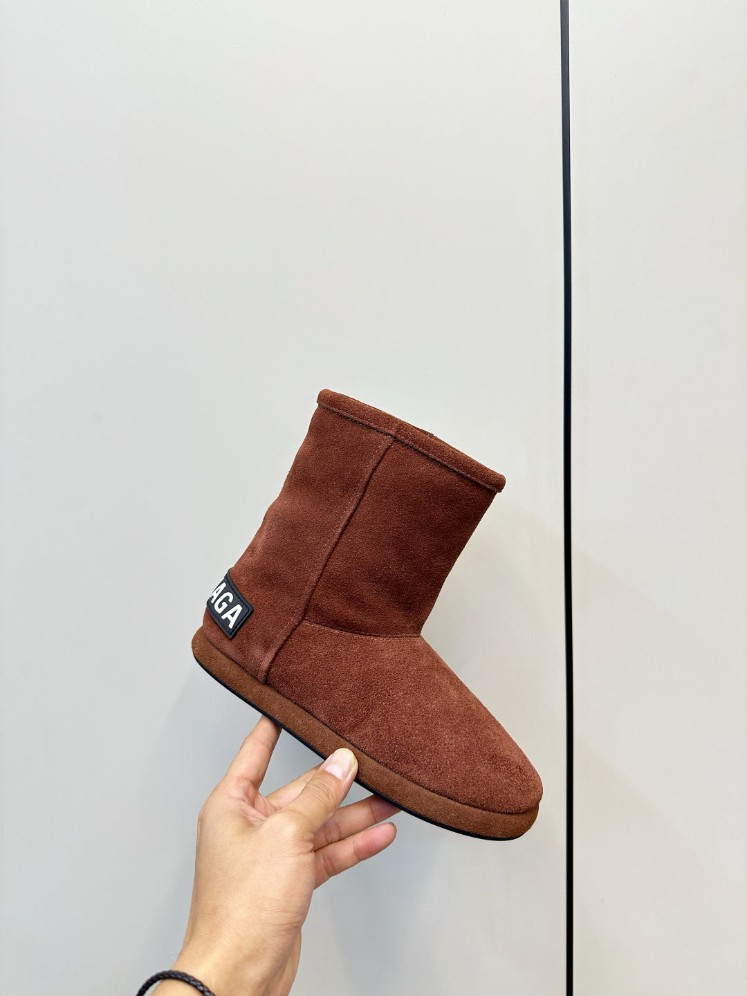 Brown suede ankle boot held in hand, padded collar with side logo patch
