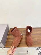 Suede ankle boots in brown, one held by hand, with small logo patch