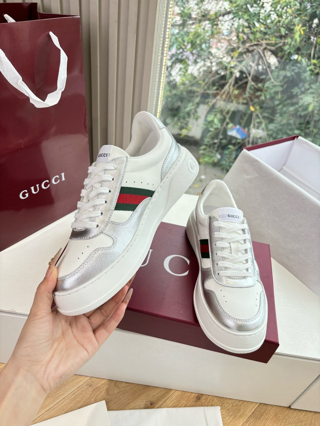 White Gucci leather sneakers, one shoe held up showing red and green side stripe