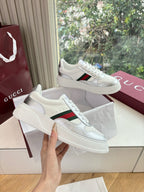 White Gucci leather sneakers, one shoe held forward showing red and green side stripe
