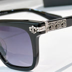 Sunglasses close-up: black square frame with silver ornate temple bar and purple-tinted lens.