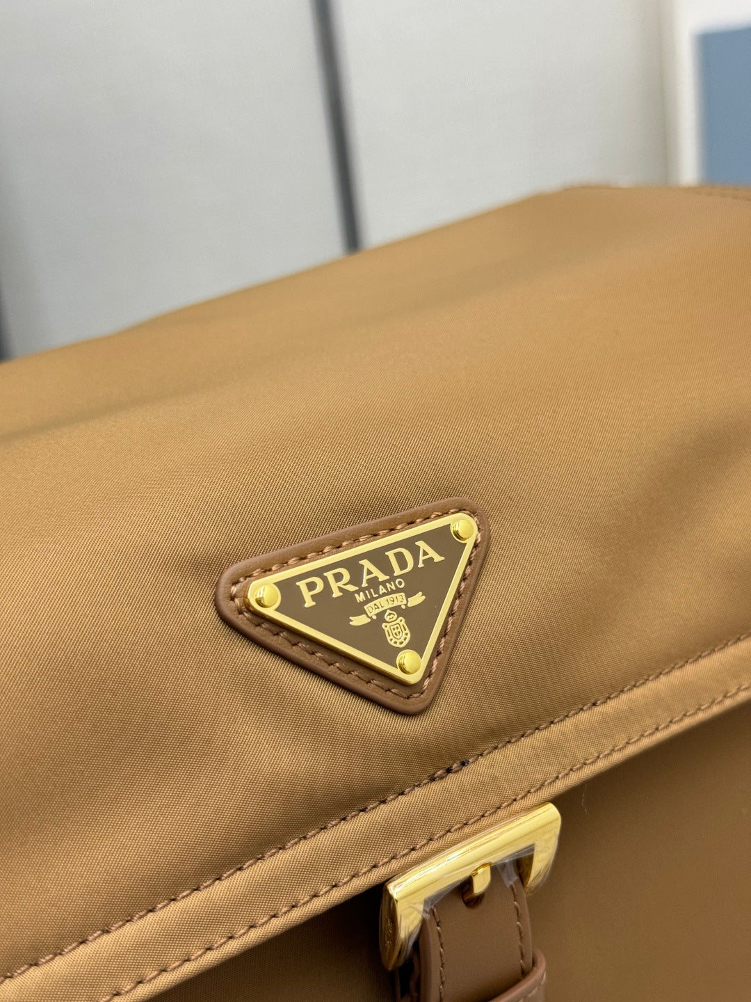 Close-up of tan flap with rectangular logo patch and gold border hardware