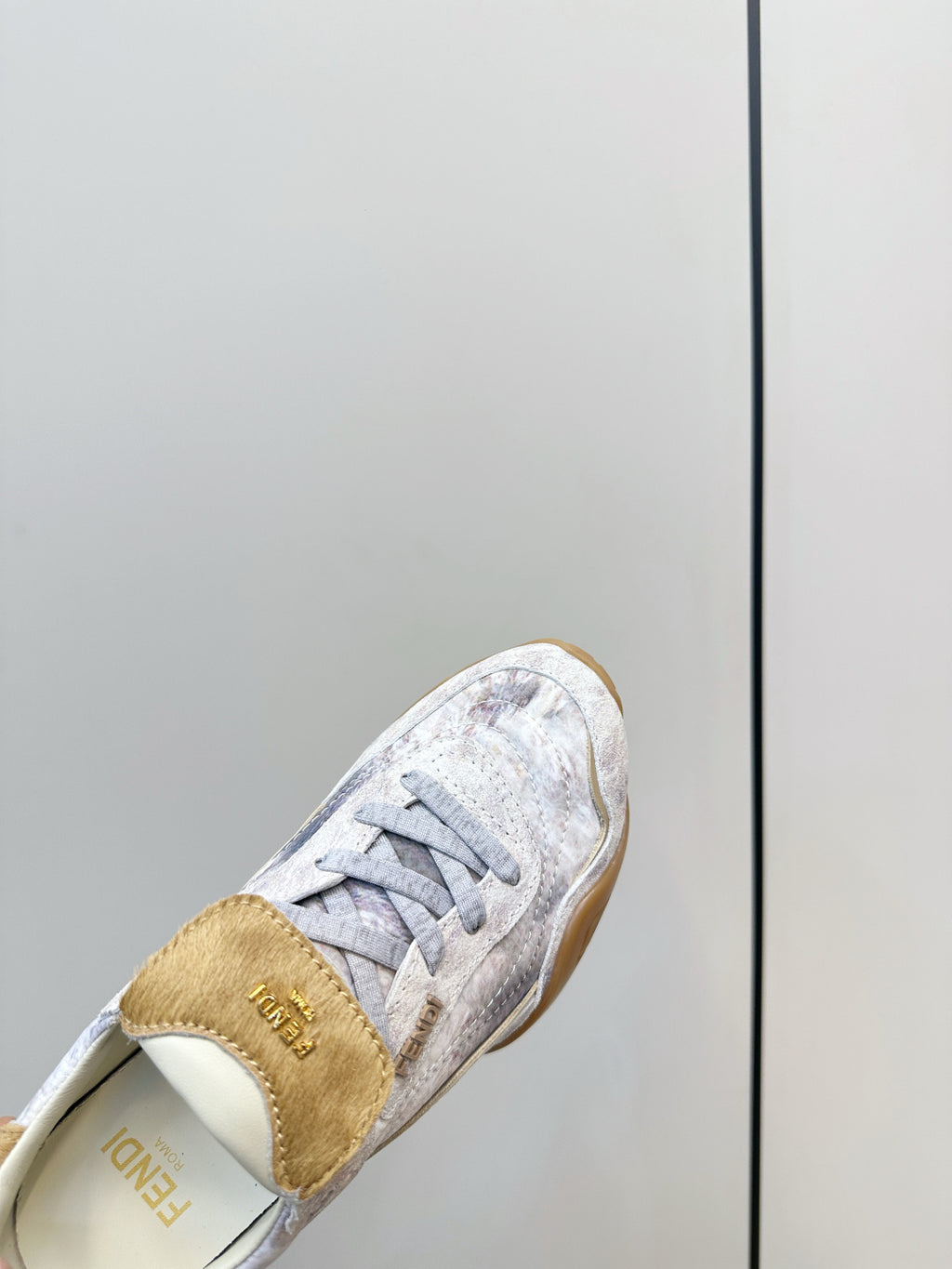 Fendi unisex sneaker close-up, tan heel tab and light gray lace-up upper.