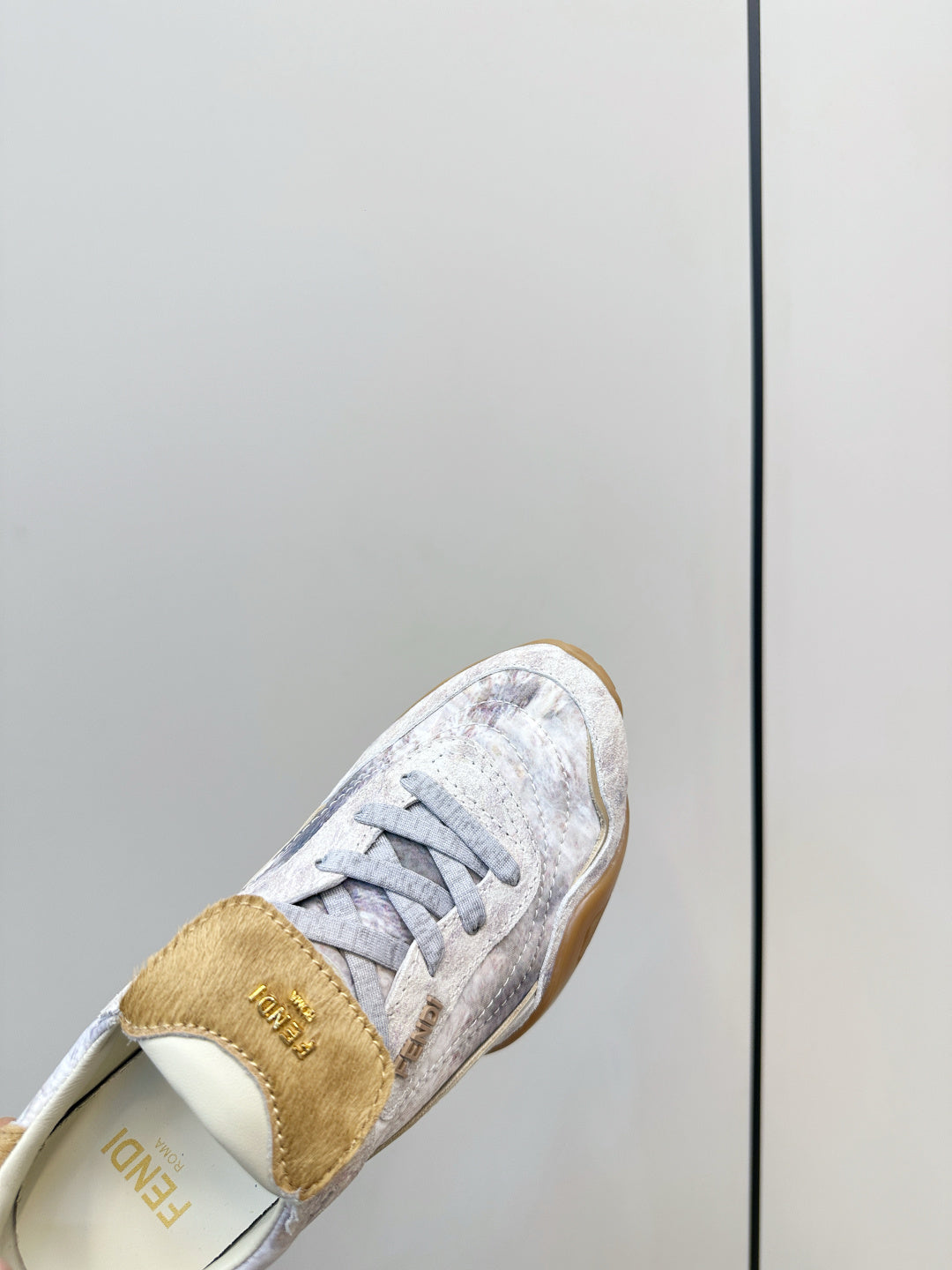 Fendi unisex sneaker close-up, tan heel tab and light gray lace-up upper.