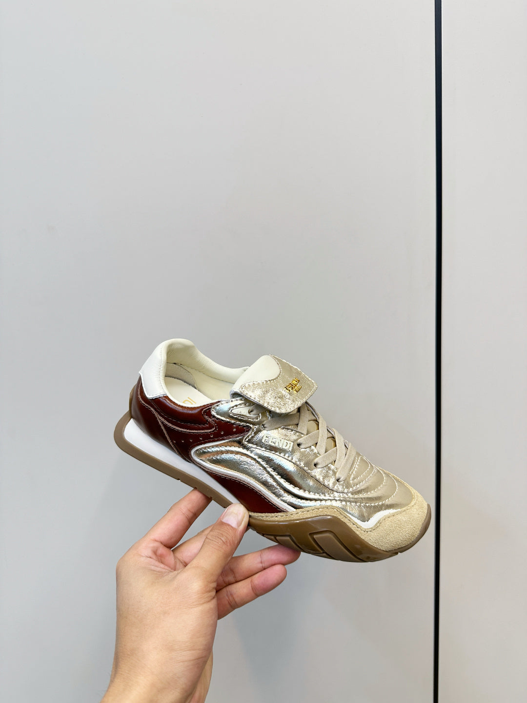 Fendi unisex sneaker held in hand, metallic gold leather with brown trim and white sole