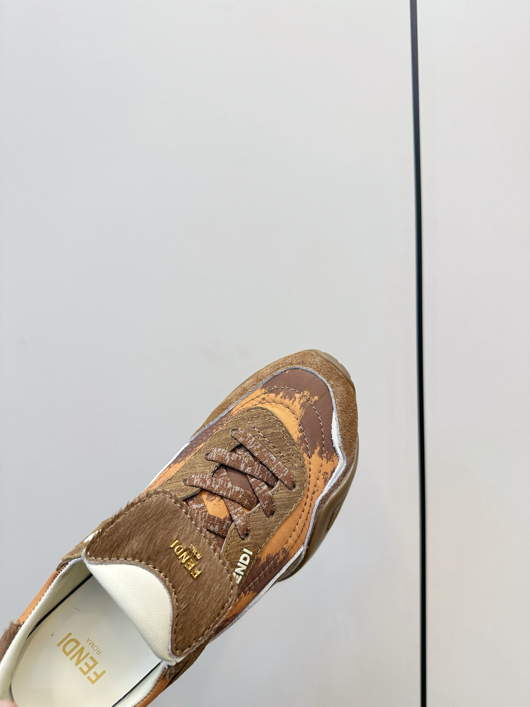 Fendi unisex sneaker close-up, brown patterned upper with lace-up front and white trim