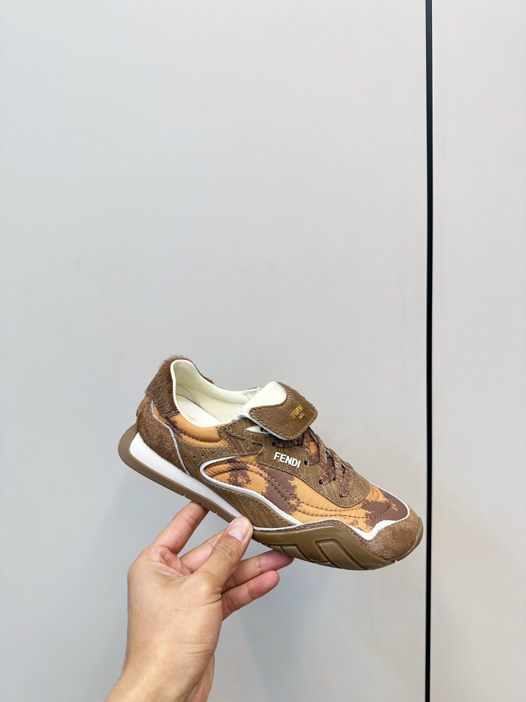 Fendi unisex sneakers held up, brown and tan patterned upper with logo on strap