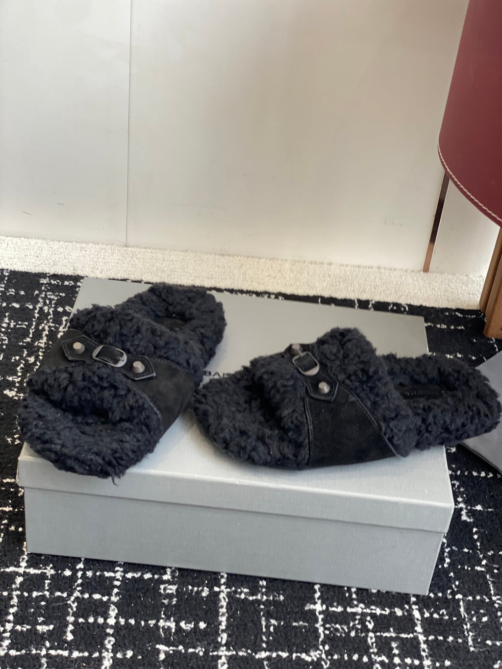 Black fuzzy slide sandals with metal buckle straps, side by side