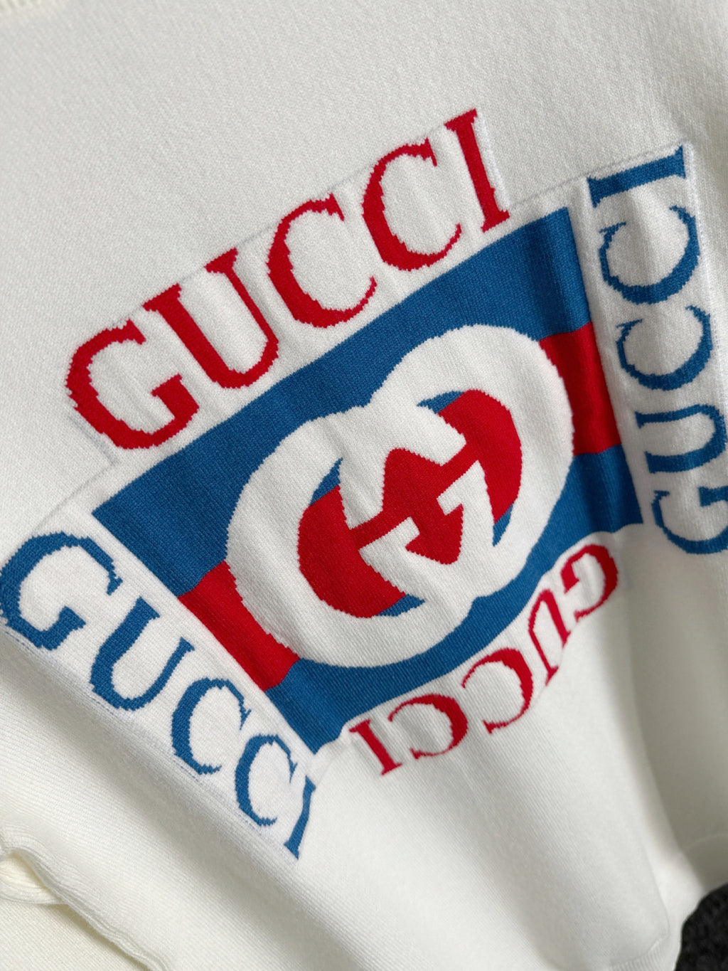 White sweatshirt fabric detail with Gucci wordmark and red/blue logo print