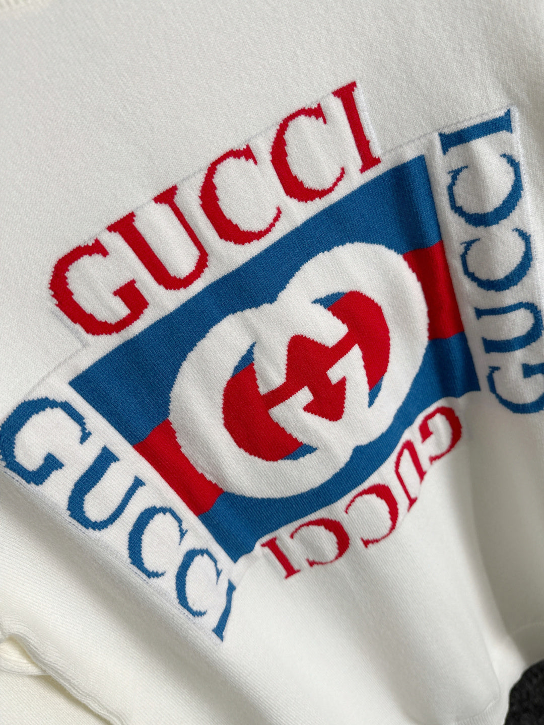 White sweatshirt fabric detail with Gucci wordmark and red/blue logo print
