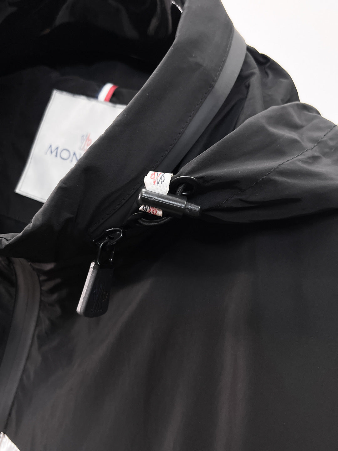 Moncler jacket front close-up with black zipper and snap, logo label visible
