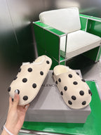 Balenciaga white polka-dot slide sandals, front view with hands holding