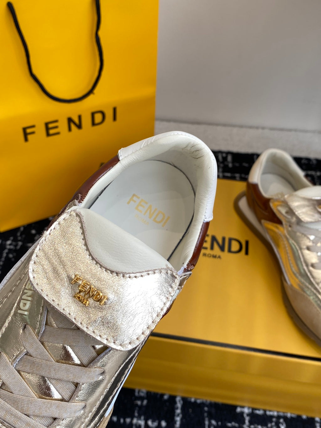 Fendi low-top sneaker: metallic silver vamp with gold-tone emblem detail.