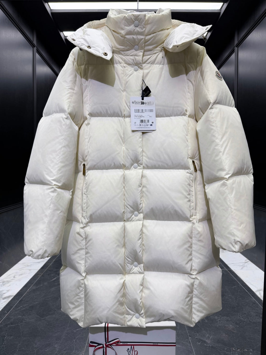 Light cream quilted puffer coat with hood, snap buttons, high collar, long sleeves.