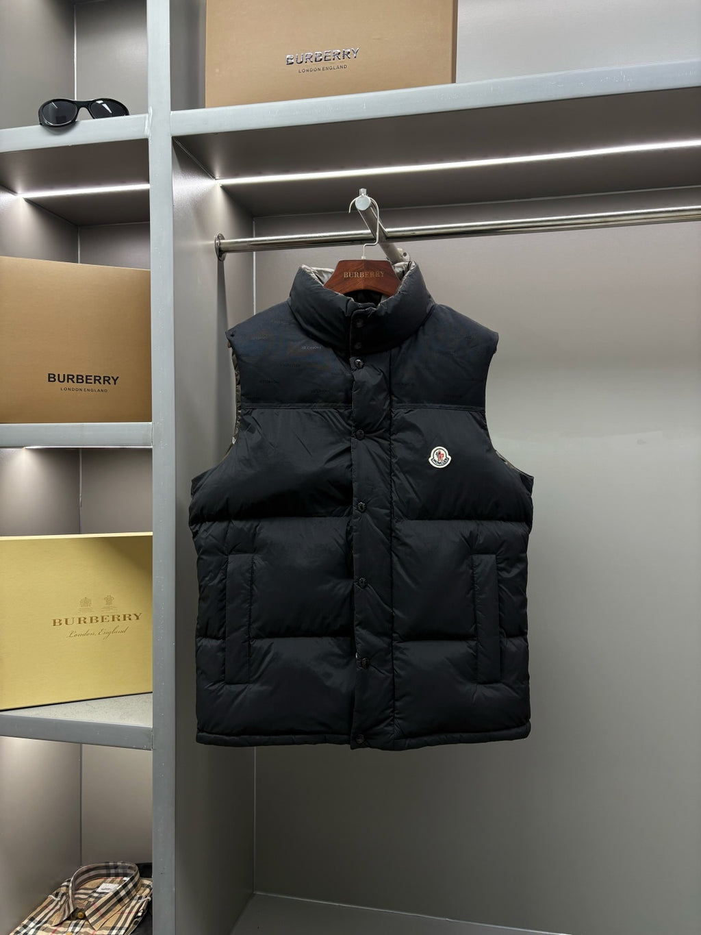 Black quilted puffer vest with button front and high stand collar, logo badge