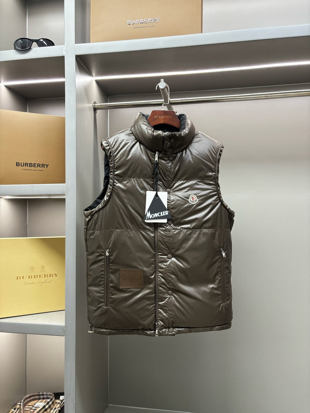 Olive long puffer vest with button front and high collar, logo patch on chest