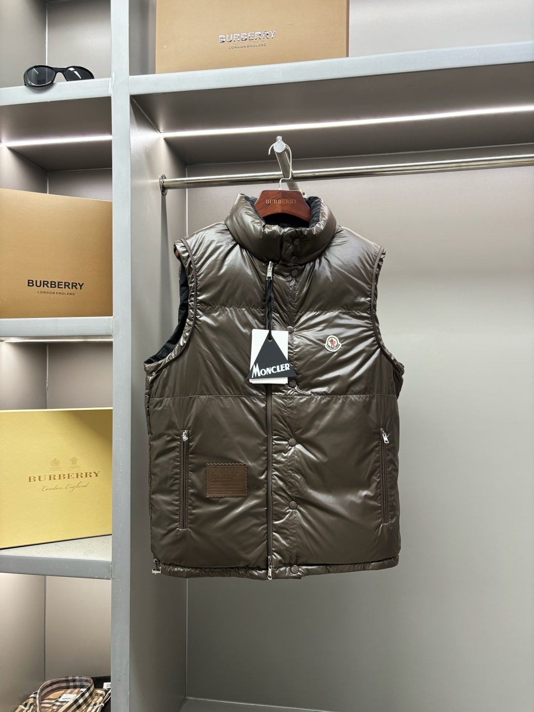 Olive long puffer vest with button front and high collar, logo patch on chest