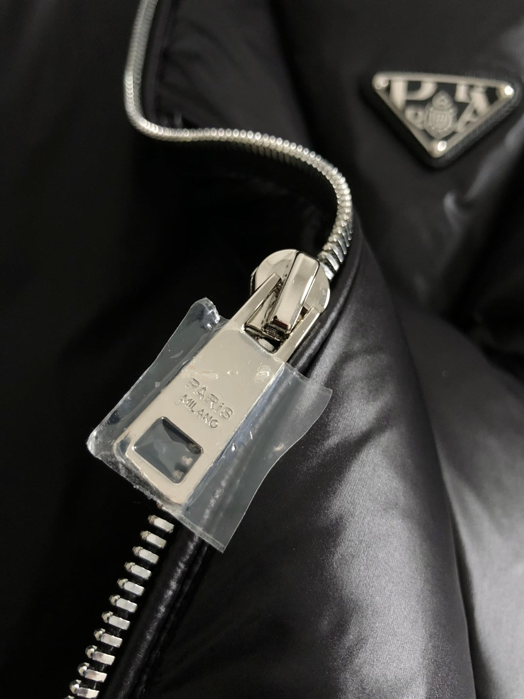 Black puffer jacket zipper close-up with Prada-branded triangular patch