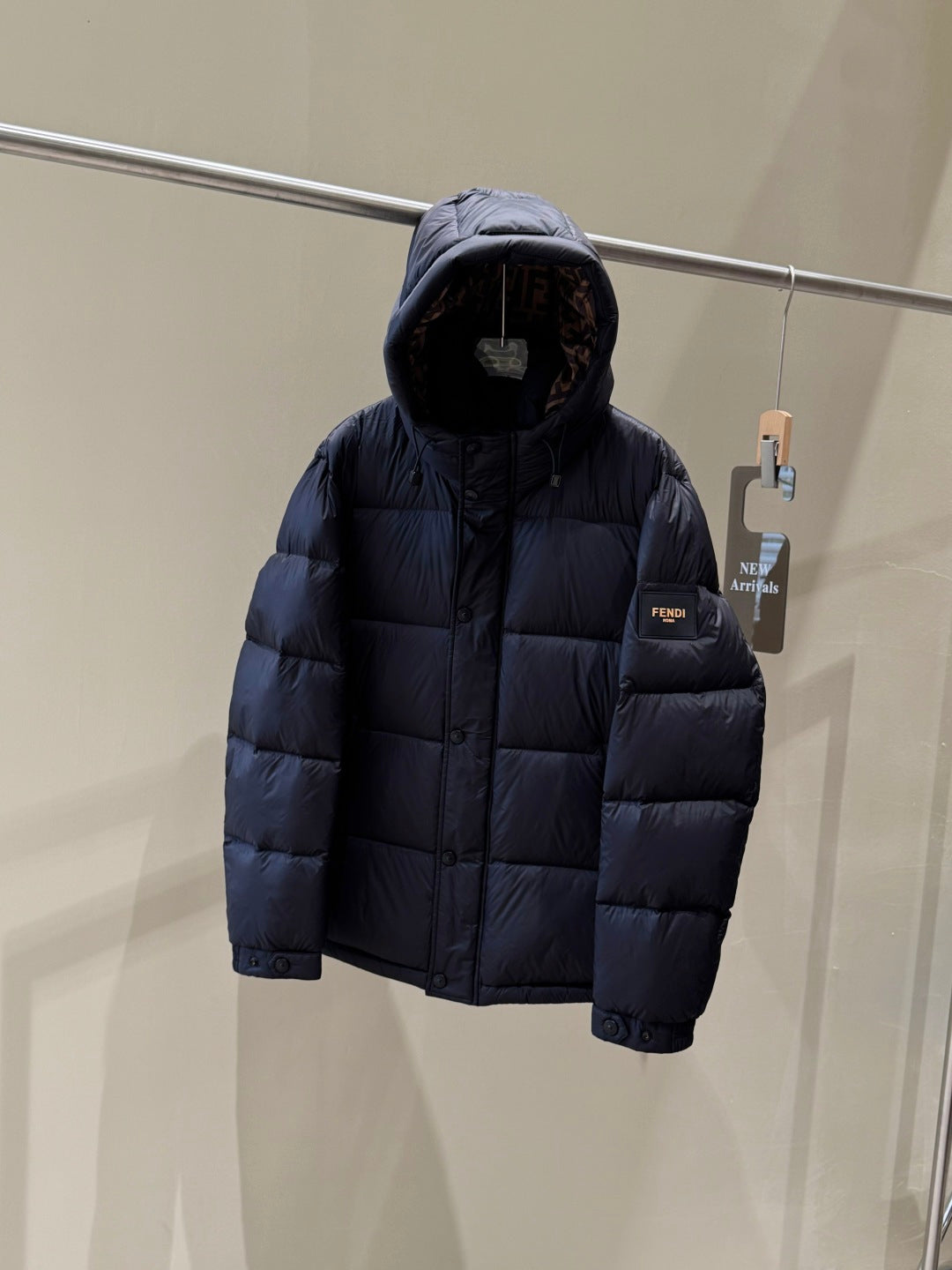 Dark hooded puffer jacket, back view with quilted panels and small logo patch.
