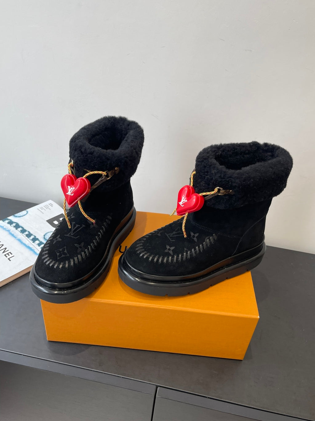 Two black monogram ankle boots with plush lining, gold laces, and red heart charms
