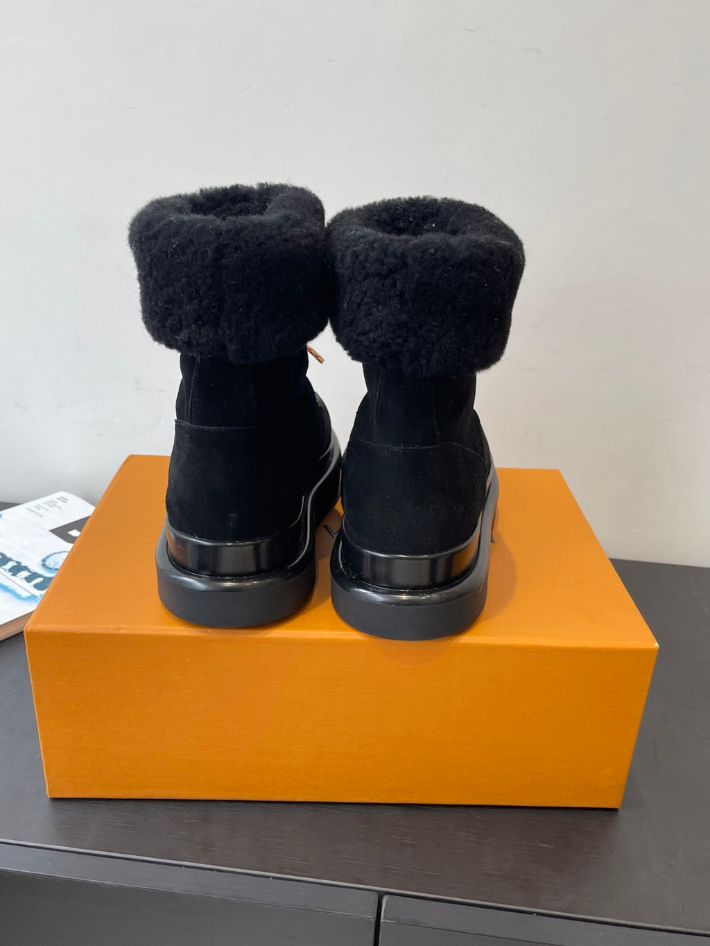 Back view of black plush ankle boots on a box, showing heel and cuffs