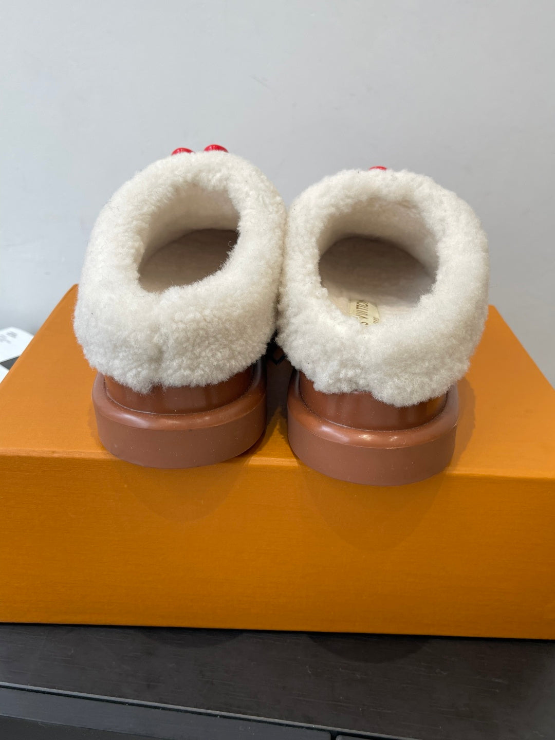 Back view of cream shearling-lined brown slip-on shoes with flat brown soles