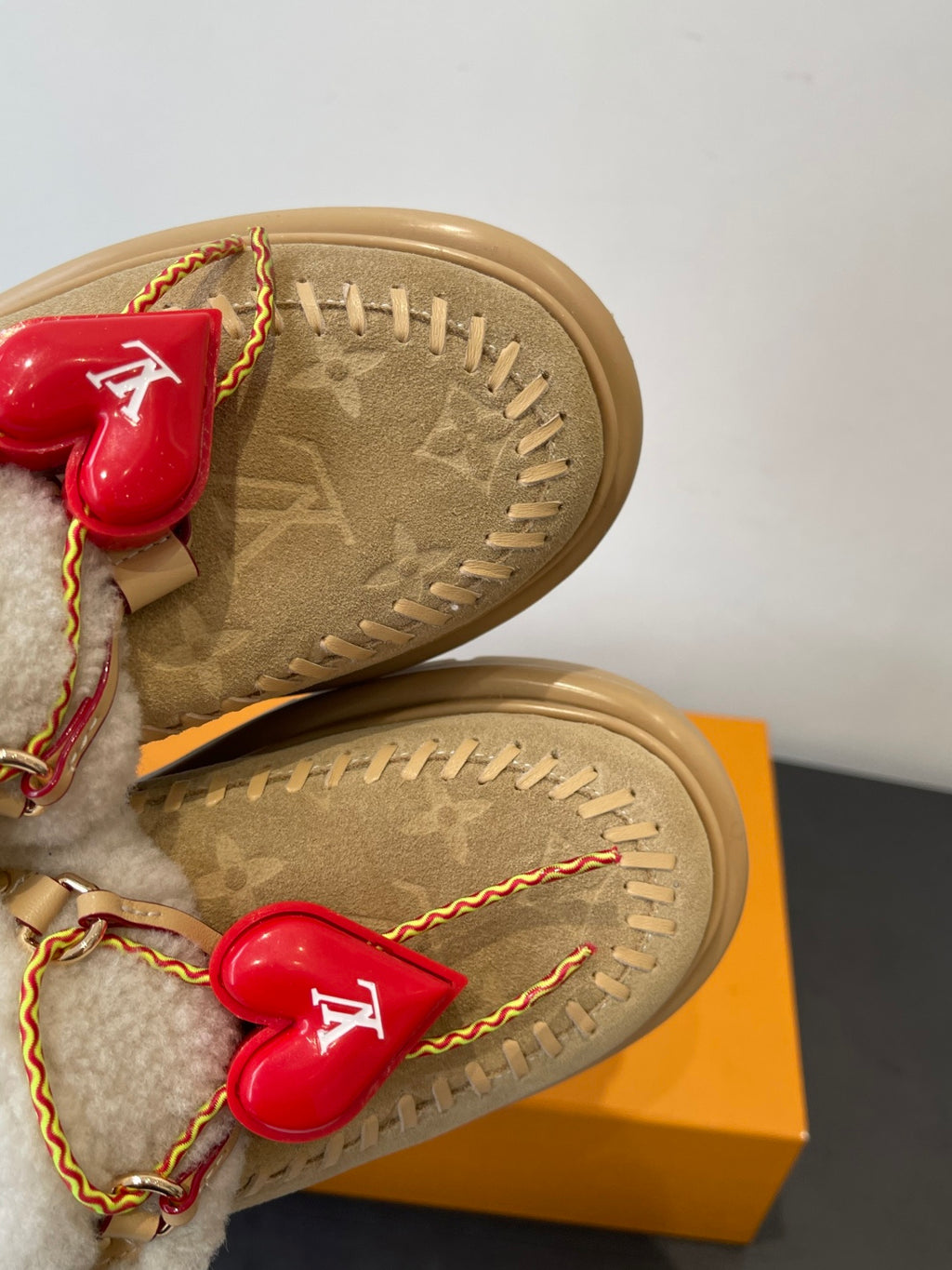 Tan shoe sole close-up with shearling straps, red heart charms and gold trim