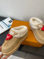 Tan shearling slip-on shoes with gold chain laces and red heart emblem charm