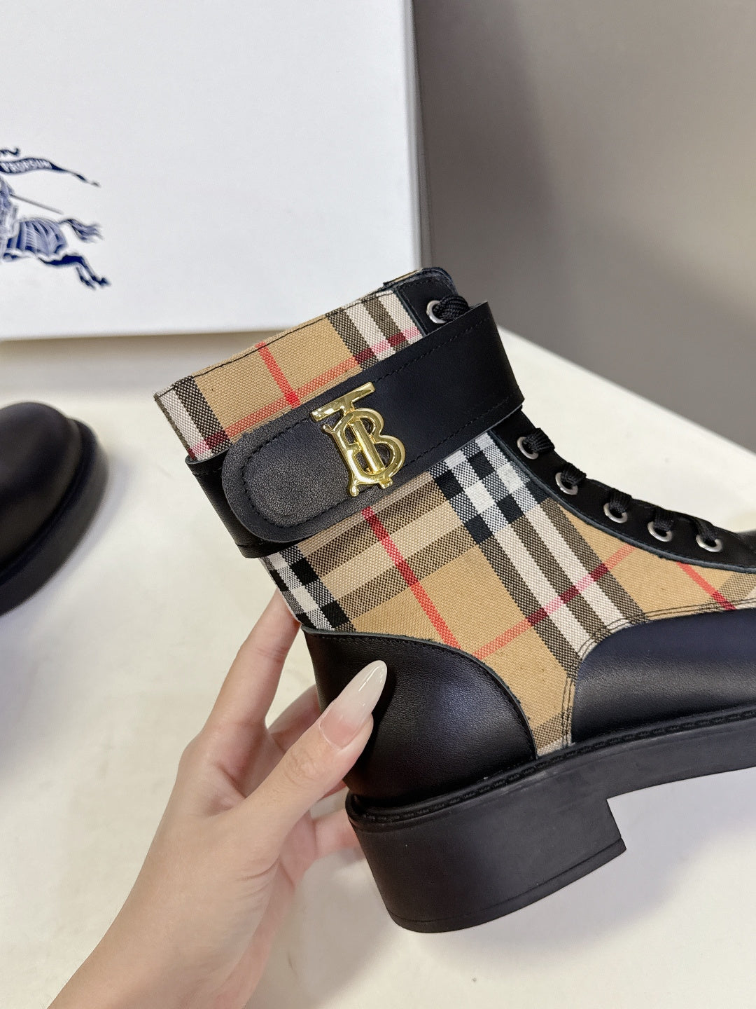 Black lace-up ankle boot with tan plaid side panel and gold TB logo buckle
