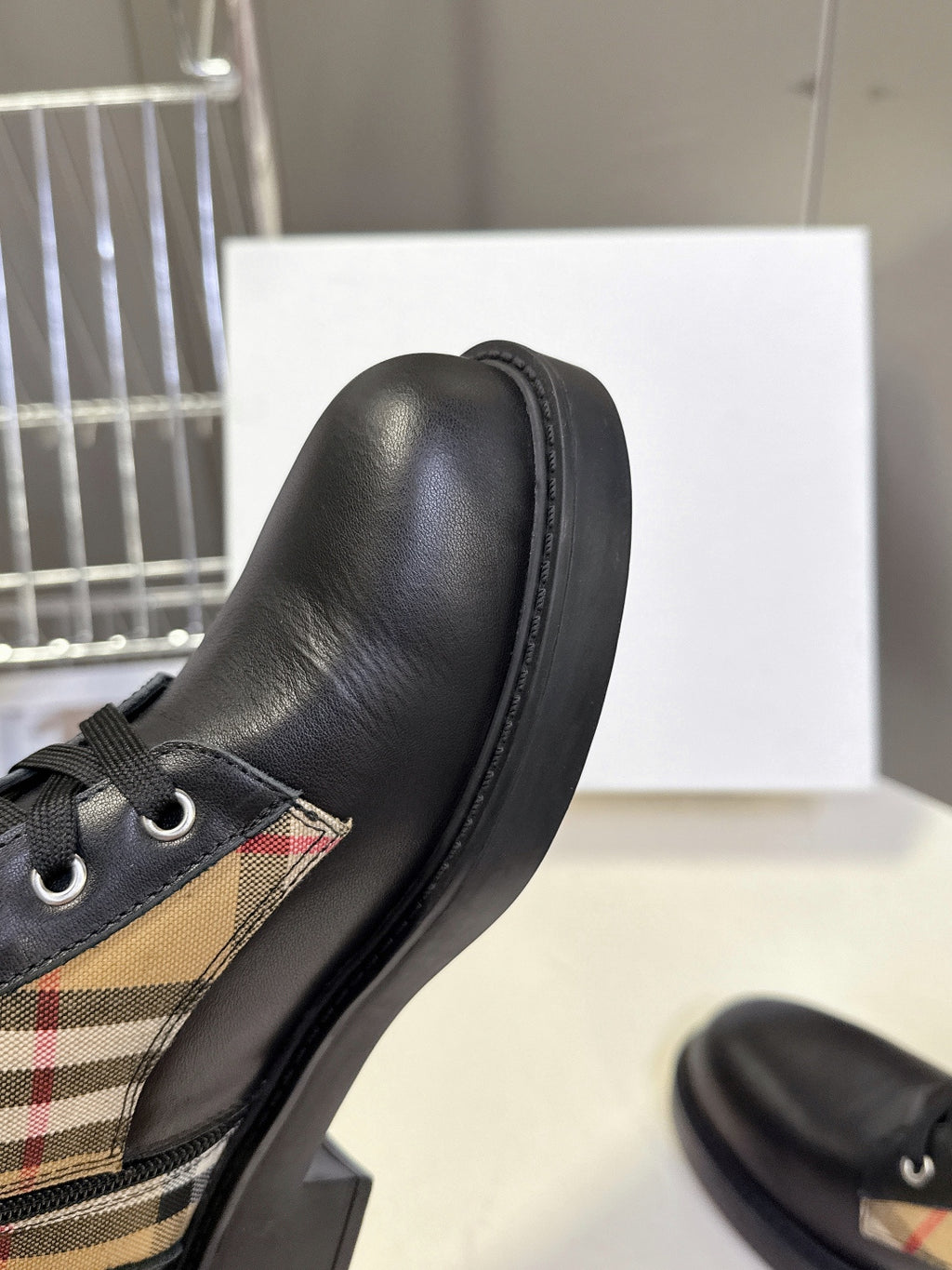 Black leather ankle boot with plaid insert near the toe and lace-up eyelets