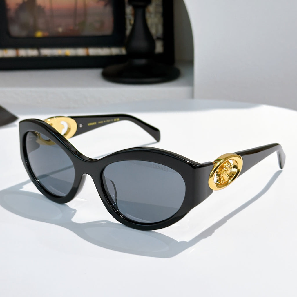Black cat-eye sunglasses with gold medallion logo detail and tinted lenses