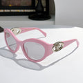 Pink cat-eye sunglasses with gold medallion logo detail and tinted lenses