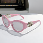 Pink cat-eye sunglasses with gold medallion logo detail and tinted lenses